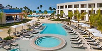 Secrets Playa Esmeralda resort pool by the beach, perfect for a destination wedding with palm trees and lounge chairs.