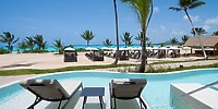 Two lounge chairs by the pool at Secrets Playa Esmeralda, perfect for a destination wedding, overlook a palm-lined beach.