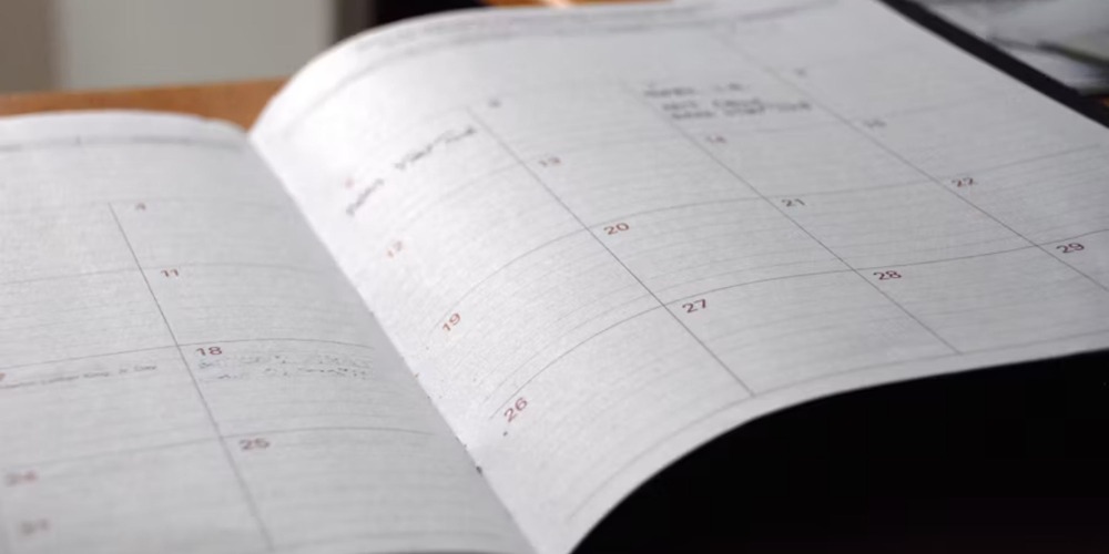 An open planner shows a monthly calendar filled with wedding notes for planning a destination wedding.