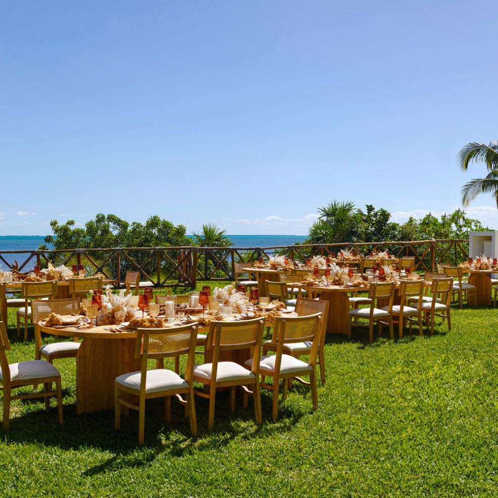 Outdoor dining tables on grass overlooking the ocean and clear sky, perfect for a destination wedding.