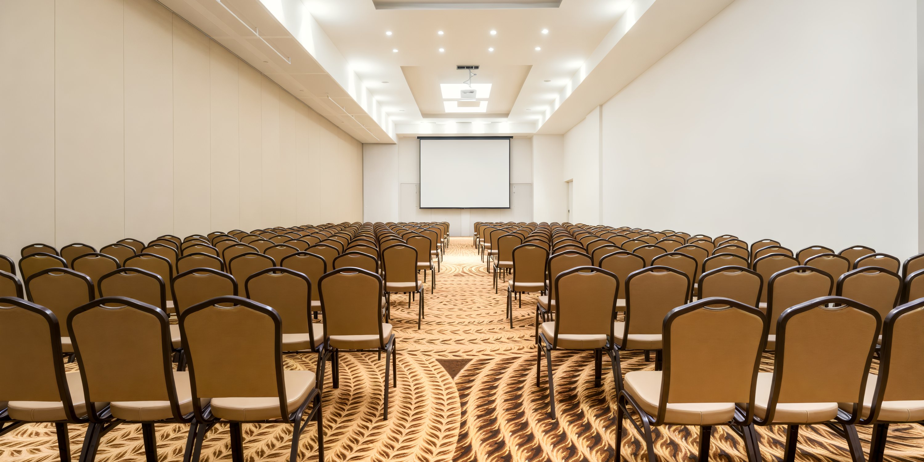 A vacant conference room featuring rows of chairs arranged towards a projection screen, reminiscent of a sophisticated setup for a destination wedding.