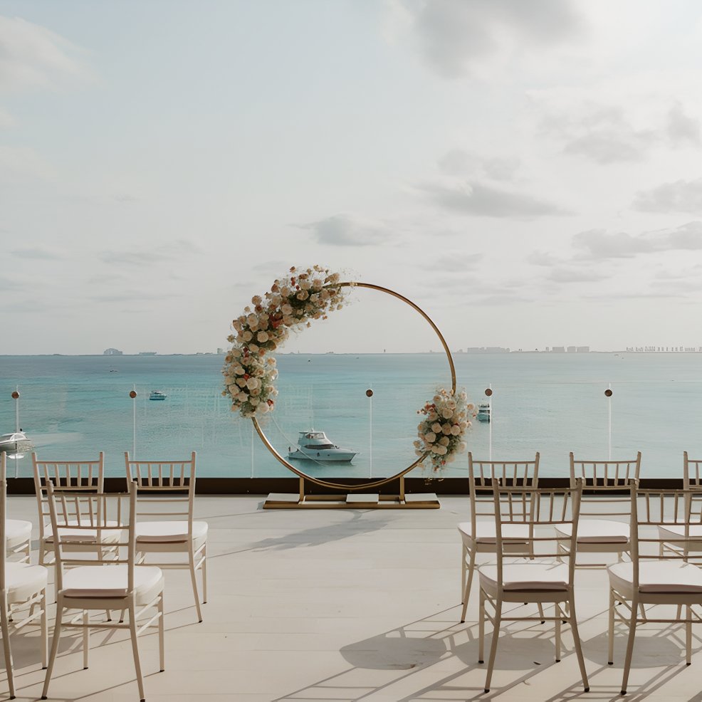 White chairs and a circular floral arch arranged for a destination wedding with ocean views.