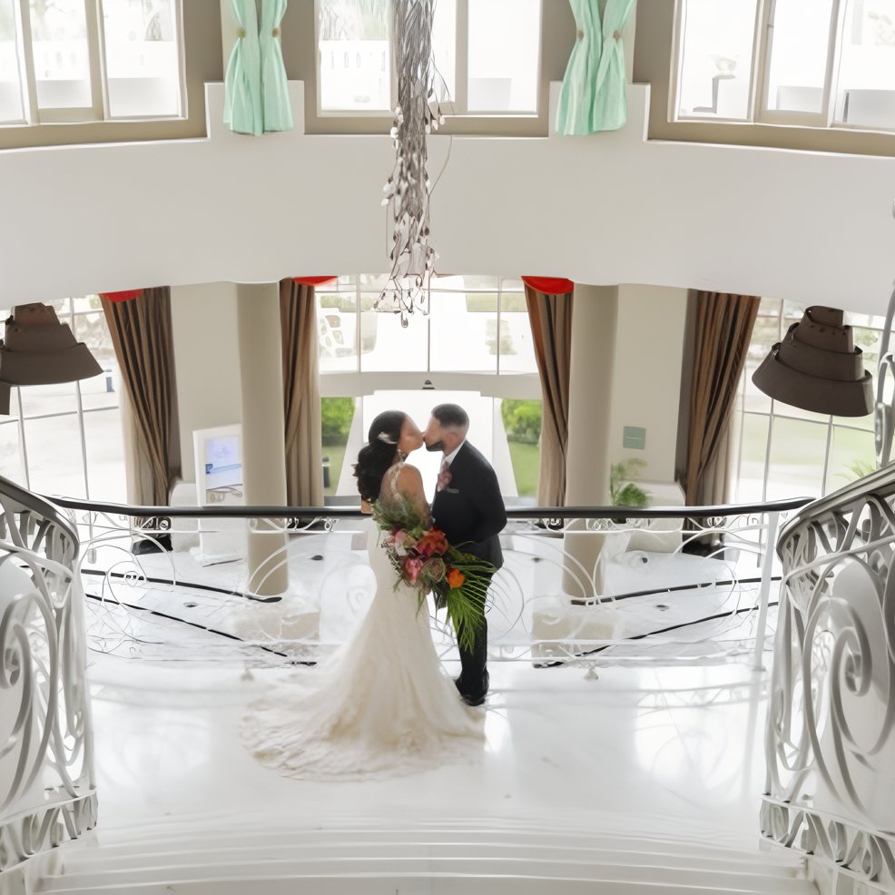 Bride and groom share a kiss on a white spiral staircase at their elegant destination wedding venue.