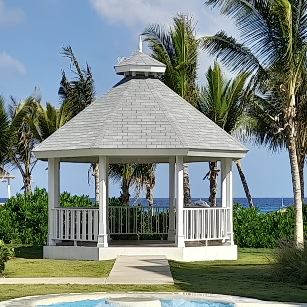 White gazebo with gray roof by palm trees, perfect for a destination wedding by the ocean.
