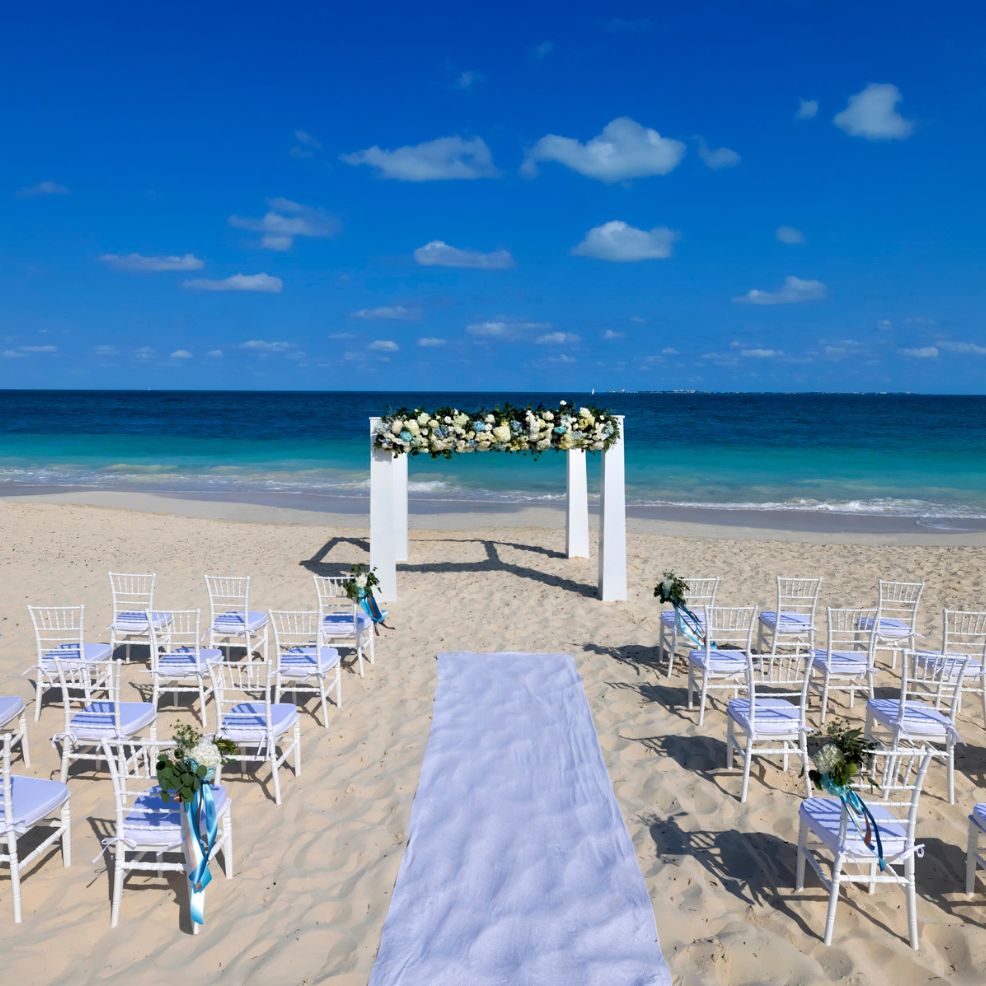 Chairs and a floral arch arranged for a destination wedding on the sandy oceanfront beach.