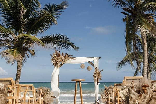 Destination wedding arch at UNICO 20&deg;105&deg;, adorned with pampas grass, on a beach among palm trees.