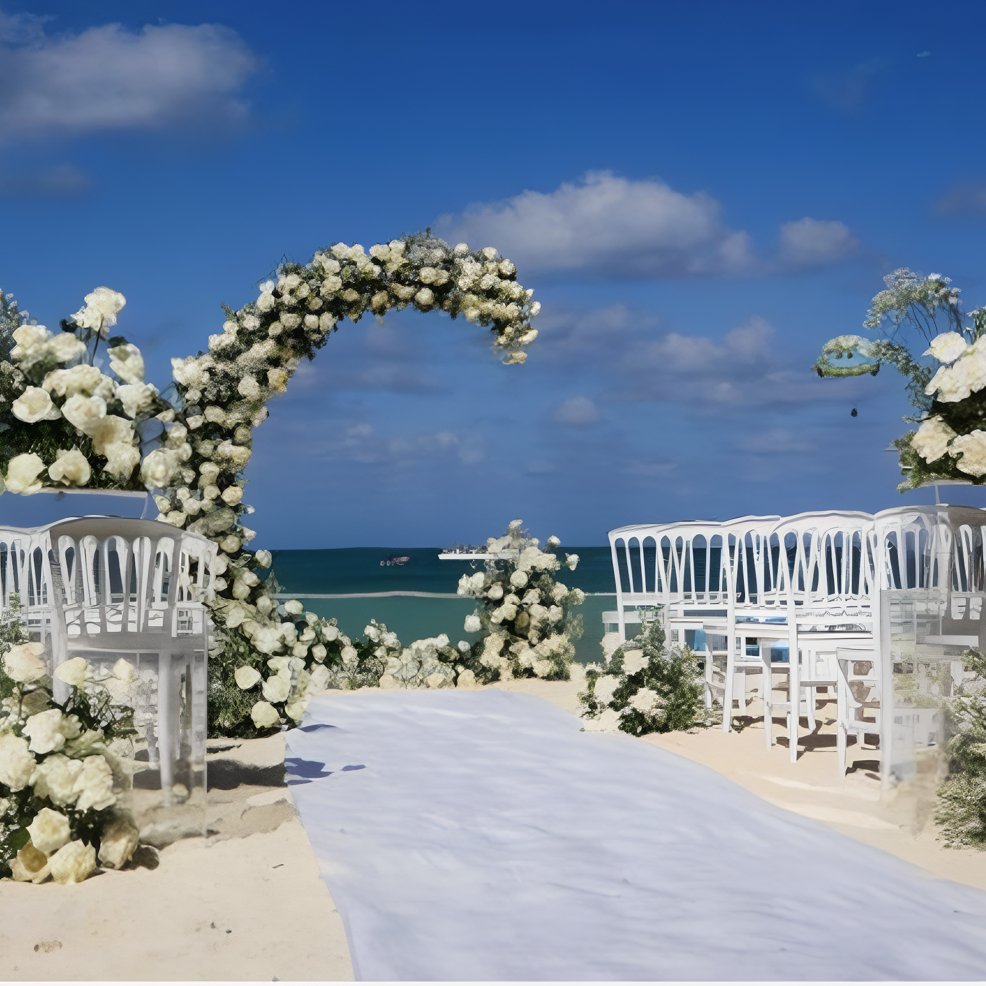 Destination wedding scene with white chairs and floral arch on the beach, ocean view and blue sky.