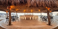 The UNICO 20°87° tiki bar, featuring a charming thatched roof, provides an inviting setting with its surrounding tables set on a tiled floor—an ideal spot for a destination wedding or a memorable wedding reception.