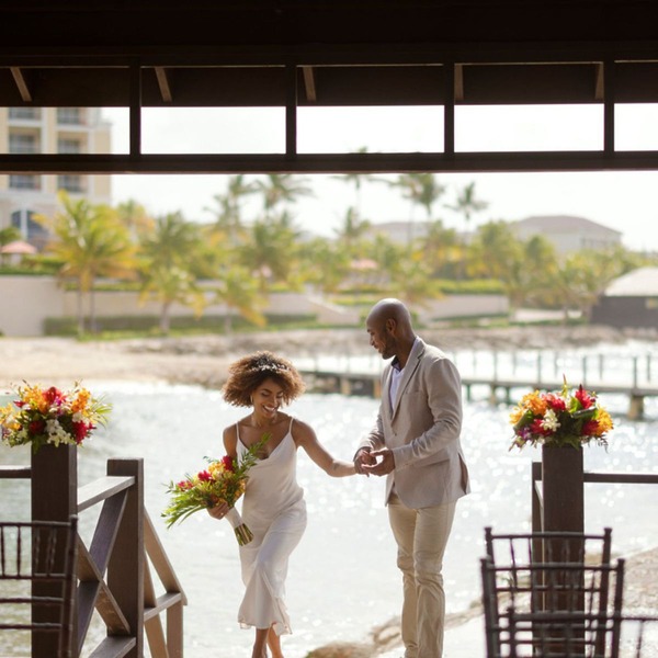 A couple strolls along the beach beneath a wooden arch, creating a romantic setting ideal for a destination wedding.