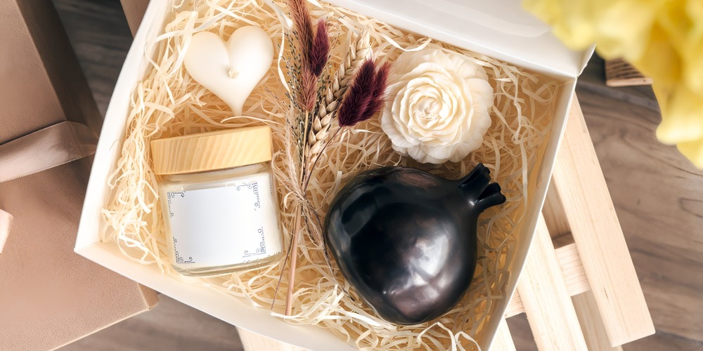 Elegant gift box for a destination wedding, featuring a scented candle, dried flowers, a white rose, dark vase, and luxurious cream container.