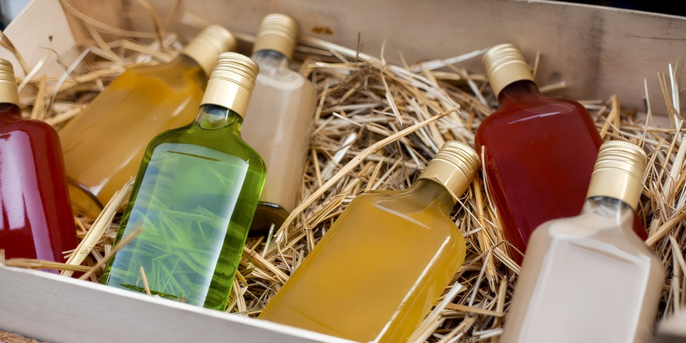Six glass bottles filled with colorful liquids are artfully arranged on straw in a rustic wooden crate, adding a charming touch to your destination wedding décor.