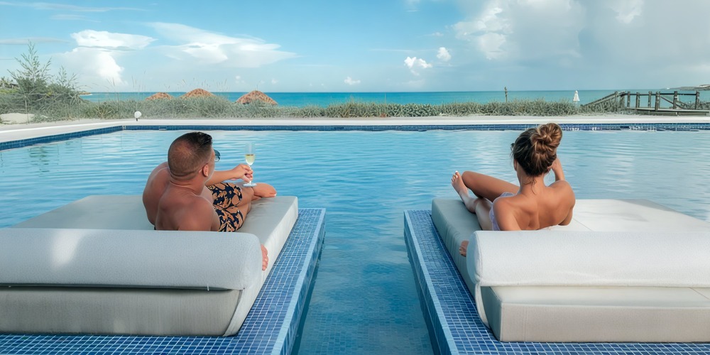 Two people relax by the poolside with drinks in hand, envisioning their perfect budget-friendly destination wedding.