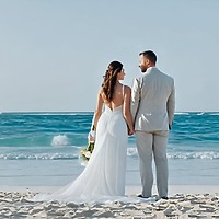Carina and Steven stand hand in hand on a sun-kissed beach, the ocean stretching before them, celebrating their destination wedding.