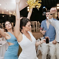 Carina and Steven dancing at a destination wedding celebration; one of them holds a drink and a gold ribbon decoration.
