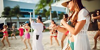 Women in swimsuits dance on the sandy beach near Hotel Riu Ventura, celebrating a destination wedding by the sea.