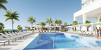 The outdoor pool at Hotel Riu Ventura, surrounded by lounge chairs and swaying palm trees under clear blue skies, offers a stunning backdrop for a destination wedding or for guests to relax before the big day.