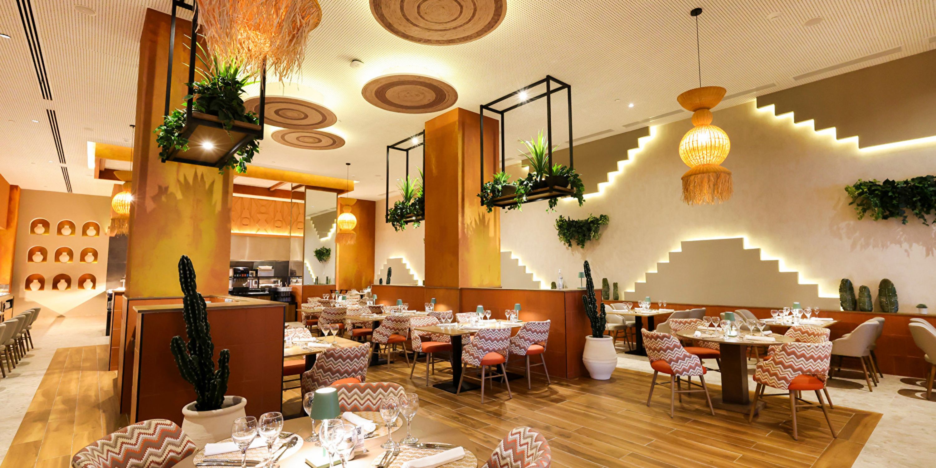 Modern interior at Hotel Riu Ventura, ideal for a destination wedding, with patterned chairs, wood tables, cacti, and warm lighting.