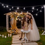 The bride and groom cut their wedding cake beneath a beautifully decorated gazebo adorned with glowing string lights, creating a magical atmosphere for their destination wedding at night.