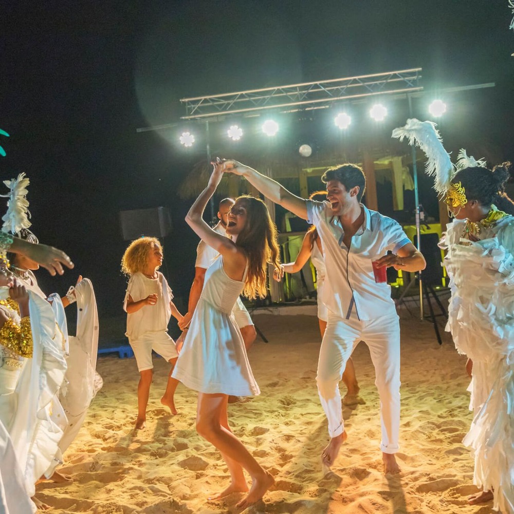 People dressed in white dance on a beach at night—an ideal scene for a destination wedding at a music-loving resort in Jamaica.