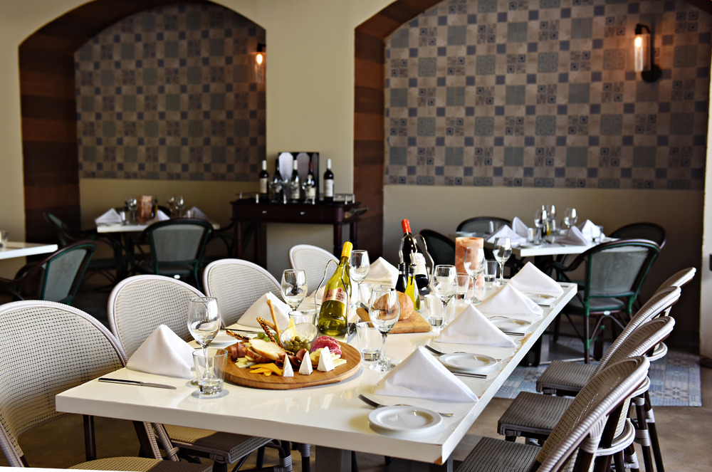 A beautifully set dining table awaits in a modern restaurant, elegantly arranged with wine, glasses, an assortment of cheeses and meats—perfect for a destination wedding celebration.
