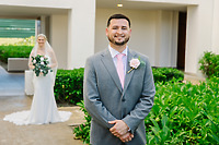 A groom beams with joy, perfectly in focus at their destination wedding, while his bride stands softly blurred in the background.