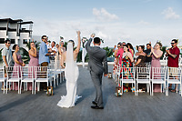 Carina and Steven walk down the aisle at their destination wedding, raising their glasses as guests stand and applaud in celebration.