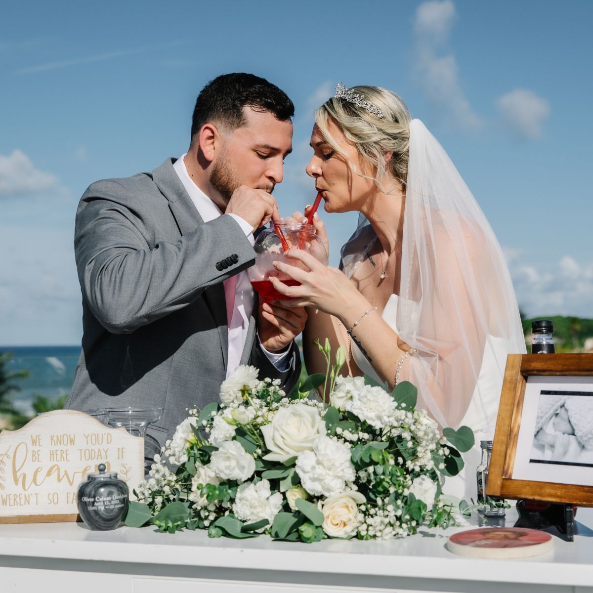 Carina and Steven enjoy a drink together at a beautifully decorated outdoor wedding table adorned with flowers and photos, soaking in the atmosphere of the destination wedding.
