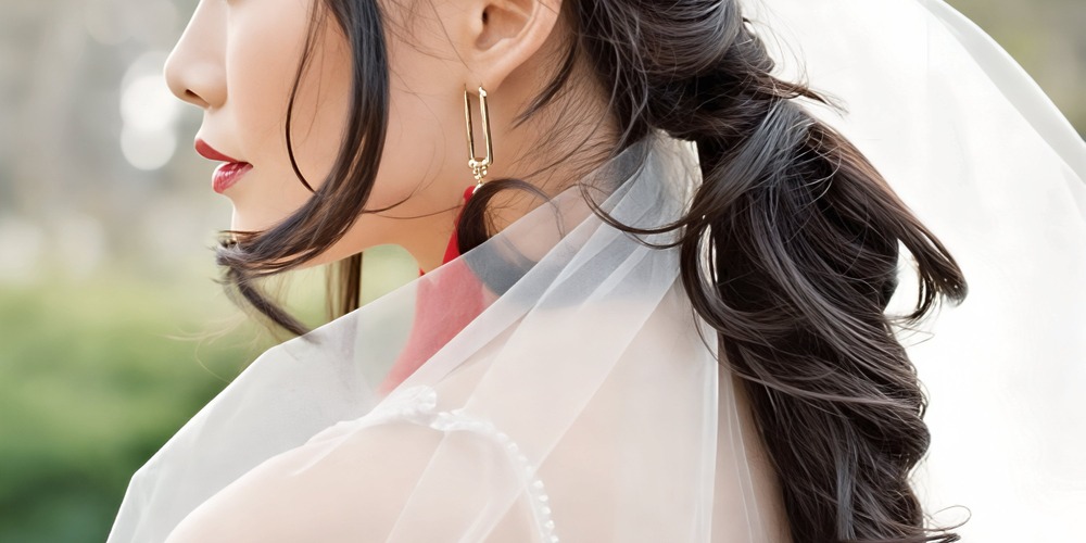 Woman with long dark hair styled in a ponytail, adorned with a wedding veil and gold earring—ideal inspiration for wedding or destination wedding hairstyles.