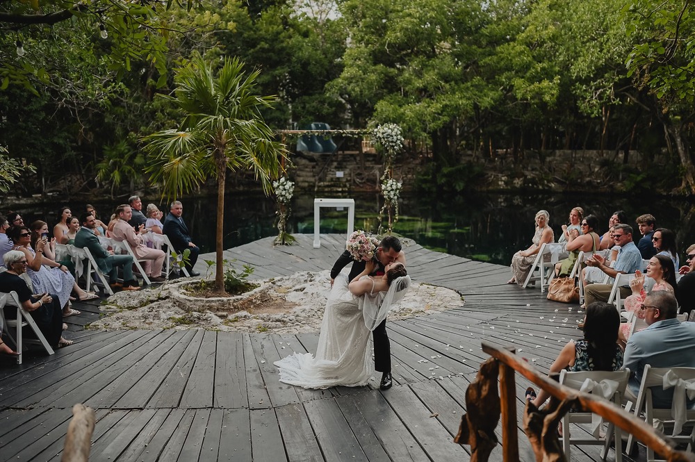 Nancy and David share a kiss at their destination wedding, surrounded by lush greenery and their guests.