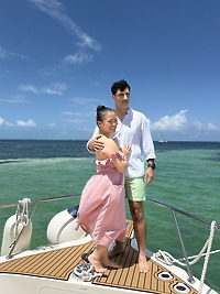 Ashleigh and Dominic stand together on the deck of a boat, the green-blue ocean sparkling behind them, capturing a perfect moment from their destination wedding.