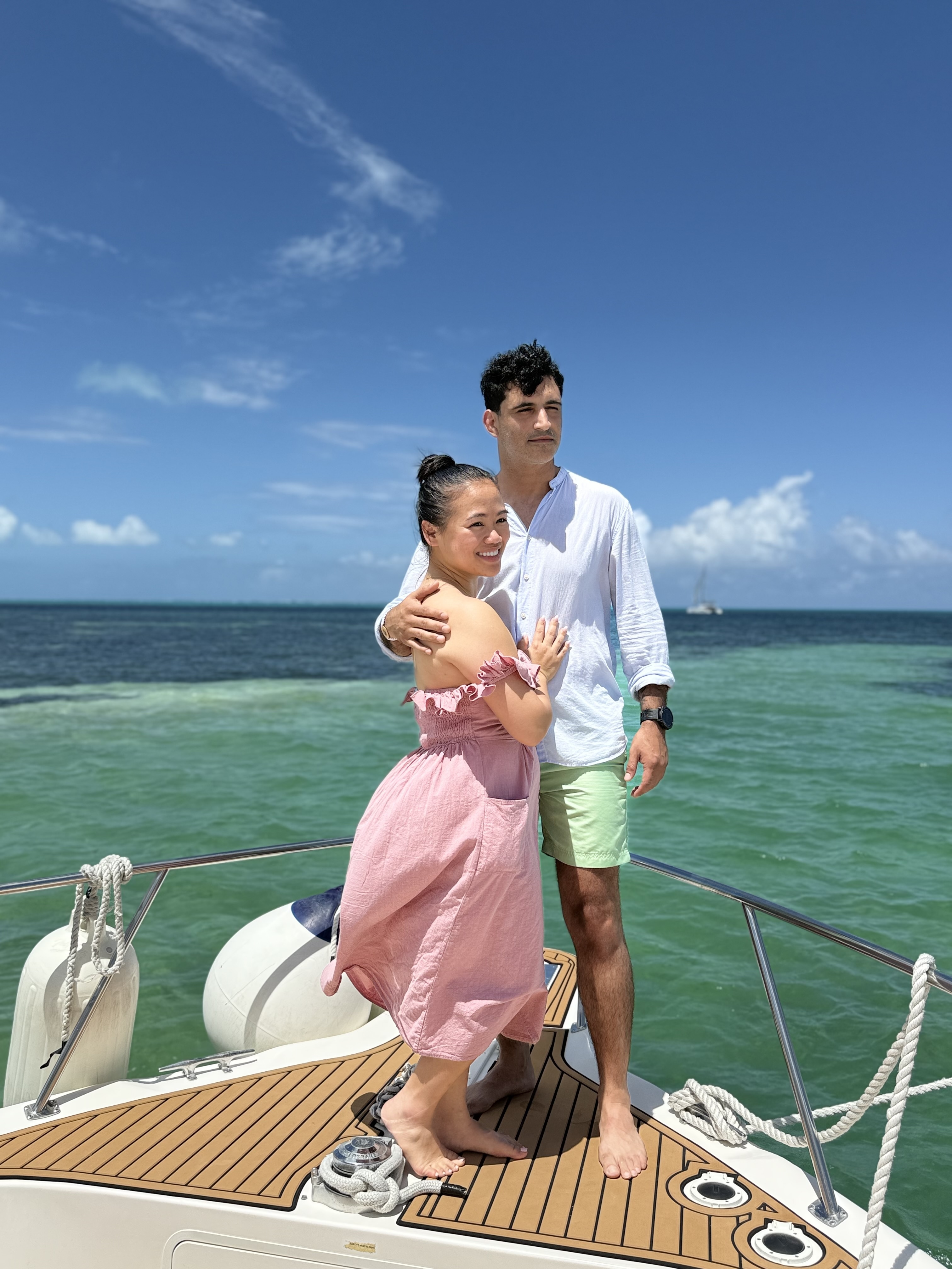 Ashleigh and Dominic stand together on the deck of a boat, the green-blue ocean sparkling behind them, capturing a perfect moment from their destination wedding.