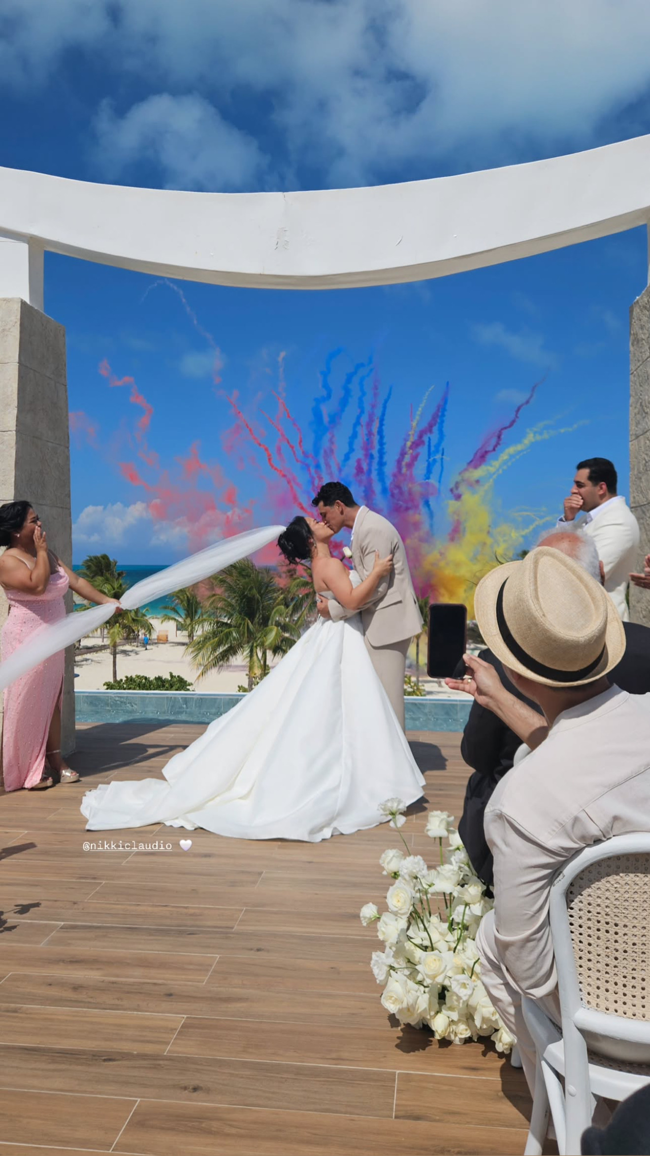 Ashleigh and Dominic share a kiss at their outdoor destination wedding, with vibrant colored smoke creating a stunning backdrop.