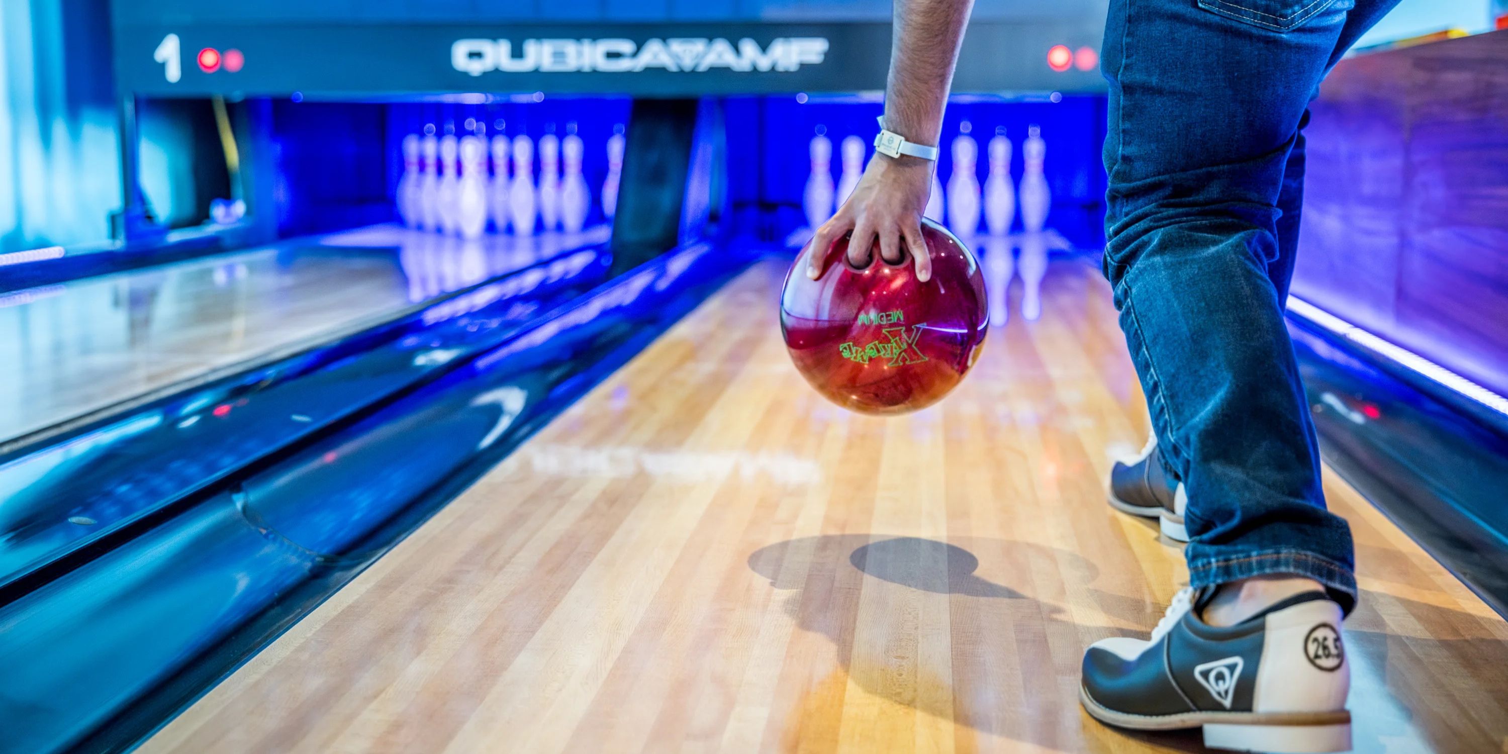 Person bowling with a red ball, shining like a destination wedding; pins lined up in the background.