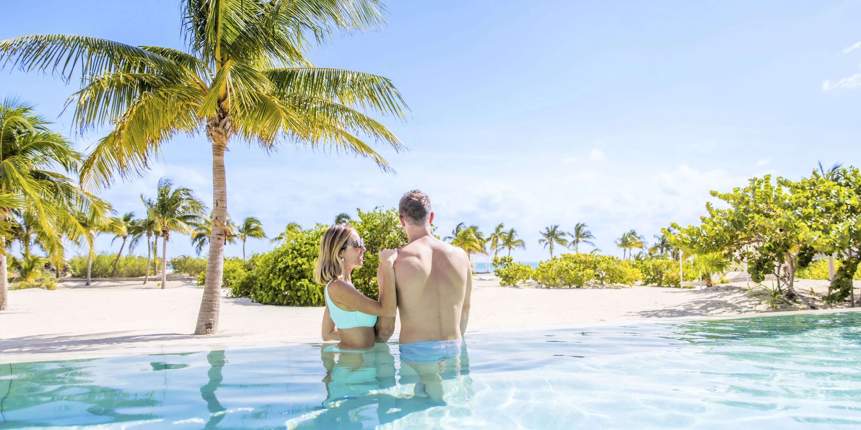 A couple enjoys the pool at their destination wedding at Majestic Mirage Costa Mujeres, palms behind them.
