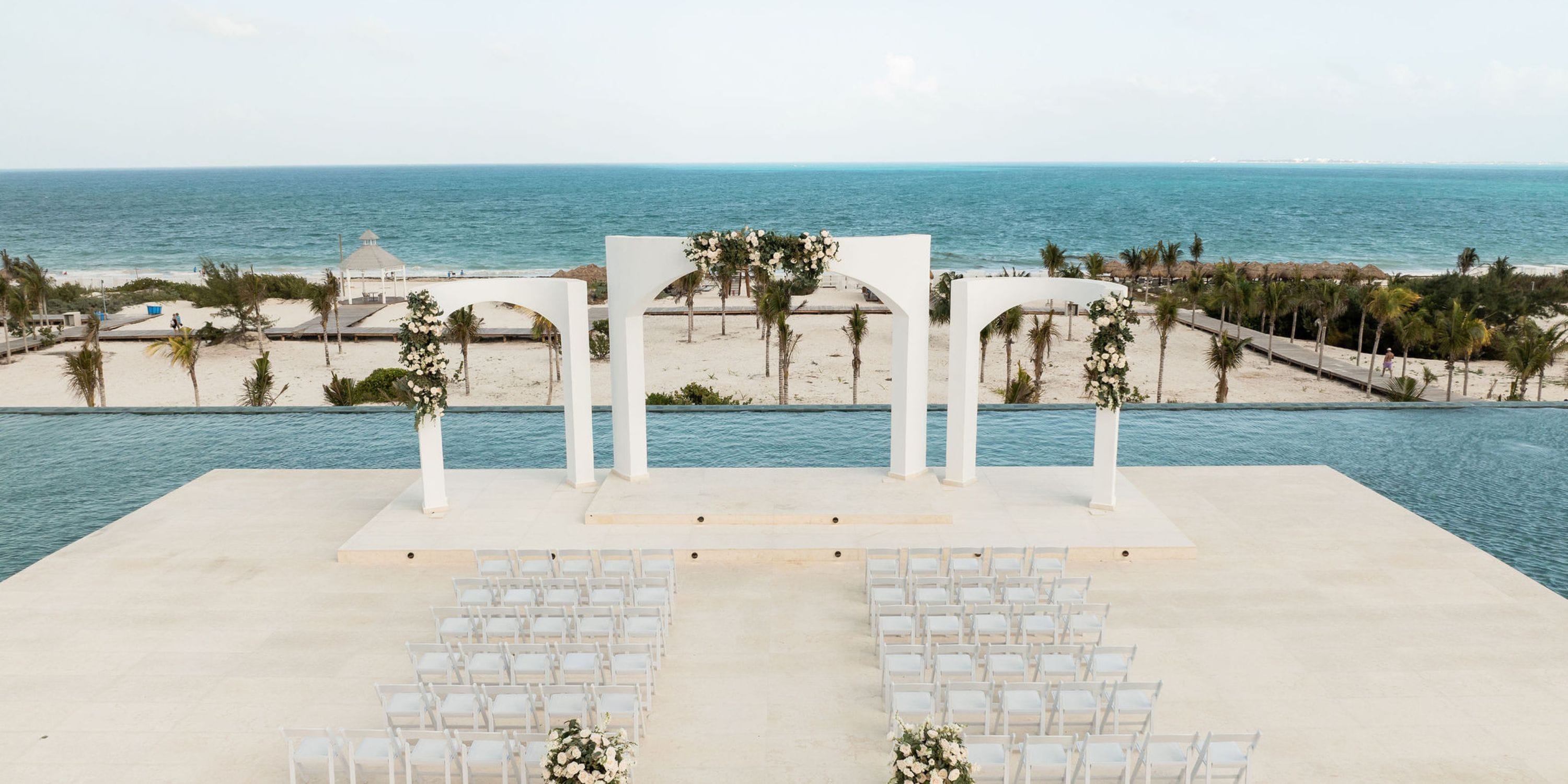 Destination wedding scene featuring white arches, chairs, and stunning Majestic Mirage Costa Mujeres views.