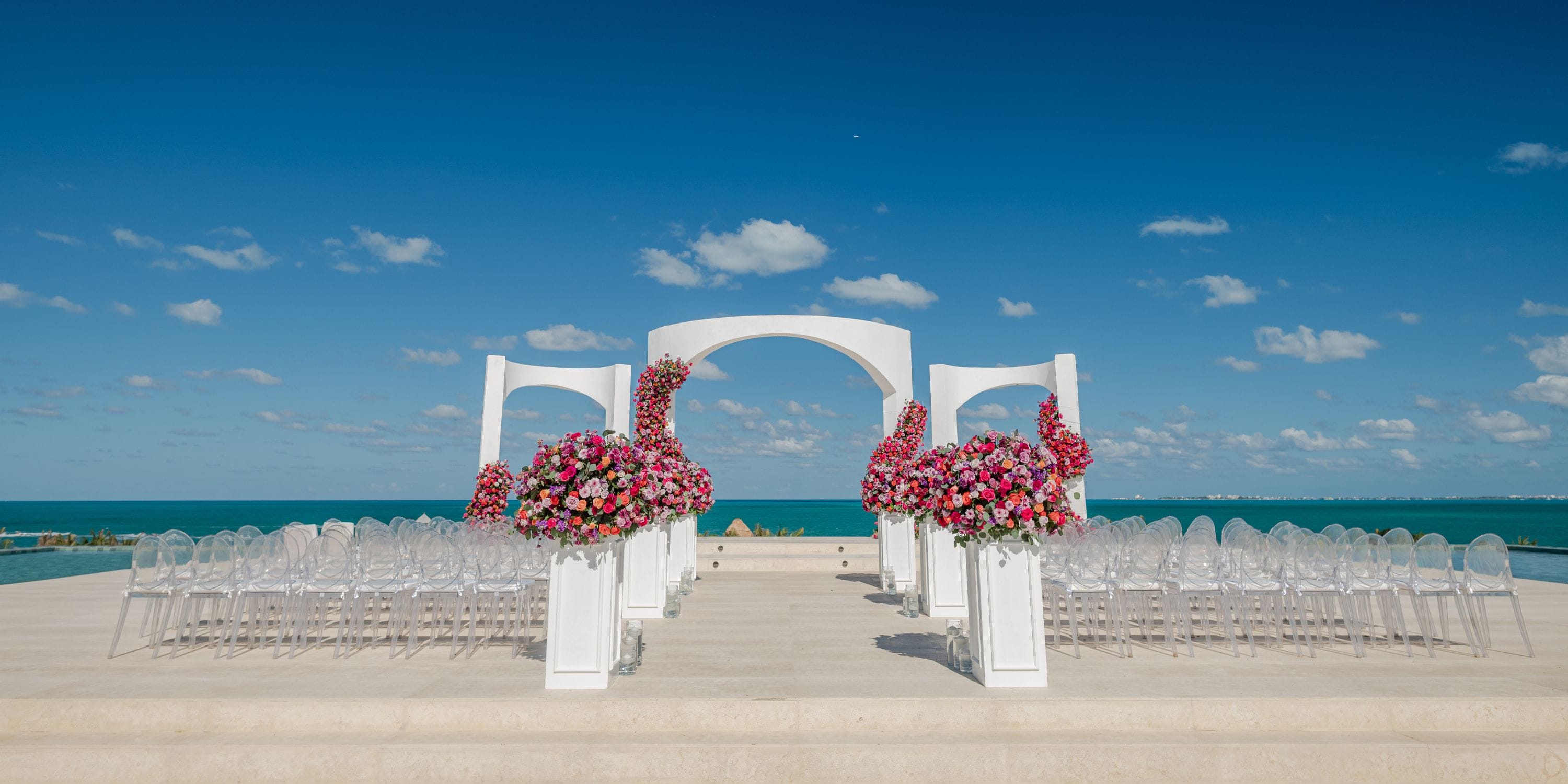 Destination wedding ceremony at Majestic Mirage Costa Mujeres, featuring a white arch and ocean backdrop.