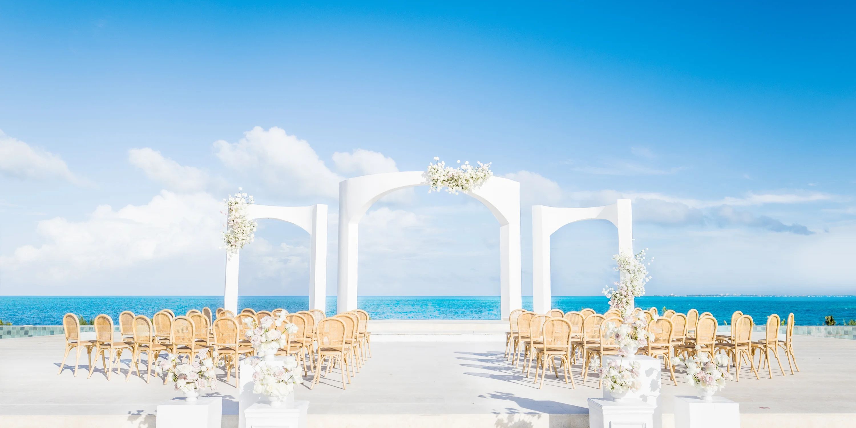 Destination wedding setup at Majestic Mirage Costa Mujeres with chairs facing a white oceanfront arch.