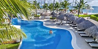 A couple enjoys the resort pool at Majestic Mirage Costa Mujeres, surrounded by palm trees and an ocean view—an ideal setting for a romantic destination wedding.