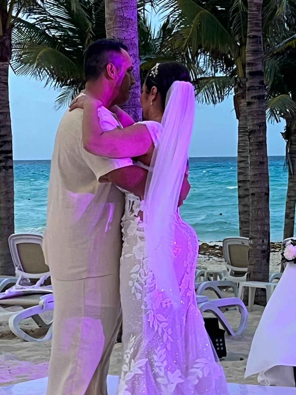 Camille and Jeff share a dance on the beach at their destination wedding, with palm trees swaying and the ocean as their backdrop.