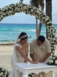 Camille and Jeff sign their wedding documents beneath a floral arch at their beautiful beachside destination wedding.