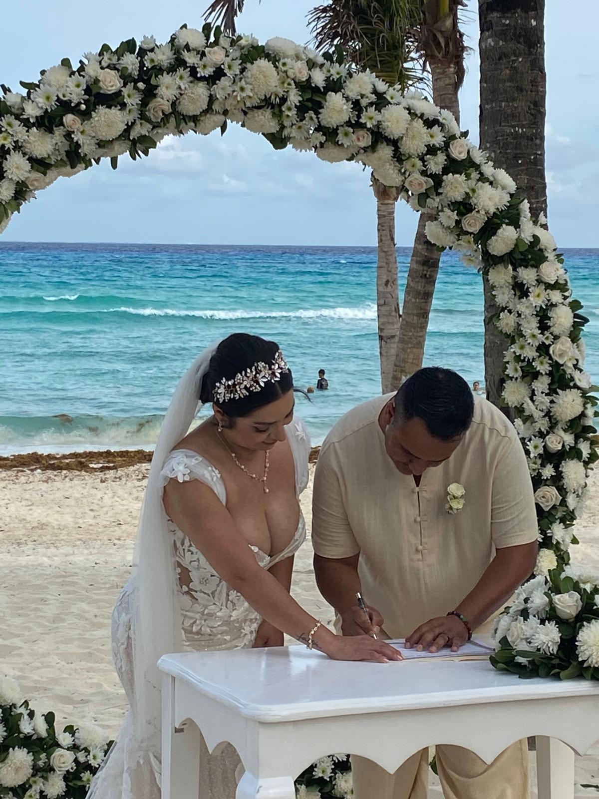Camille and Jeff sign their wedding documents beneath a floral arch at their beautiful beachside destination wedding.