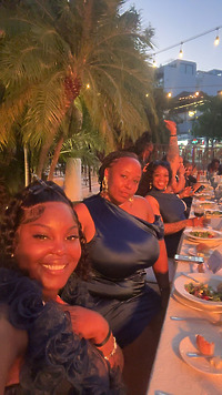Women in elegant navy dresses, perfect for a destination wedding, dine outdoors with fresh salads, surrounded by palm trees.