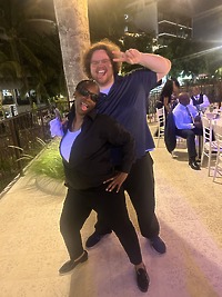 Grace and Mohammed strike a playful pose at an outdoor destination wedding, with decorated tables visible in the background.