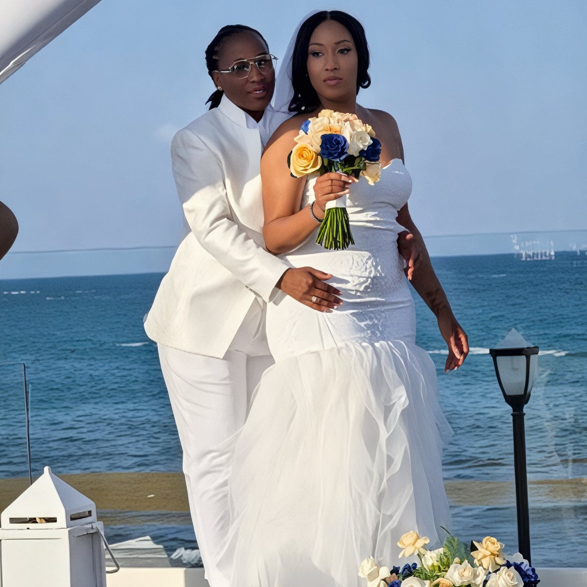 Grace and Mohammed (Copy): Two women in wedding attire pose together by the ocean, capturing a beautiful moment at their destination wedding.