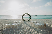 Aubrey and Noah (Copy): Rows of white chairs and a beautiful floral arch are arranged by the ocean, creating a stunning setting for a destination wedding on the beach.
