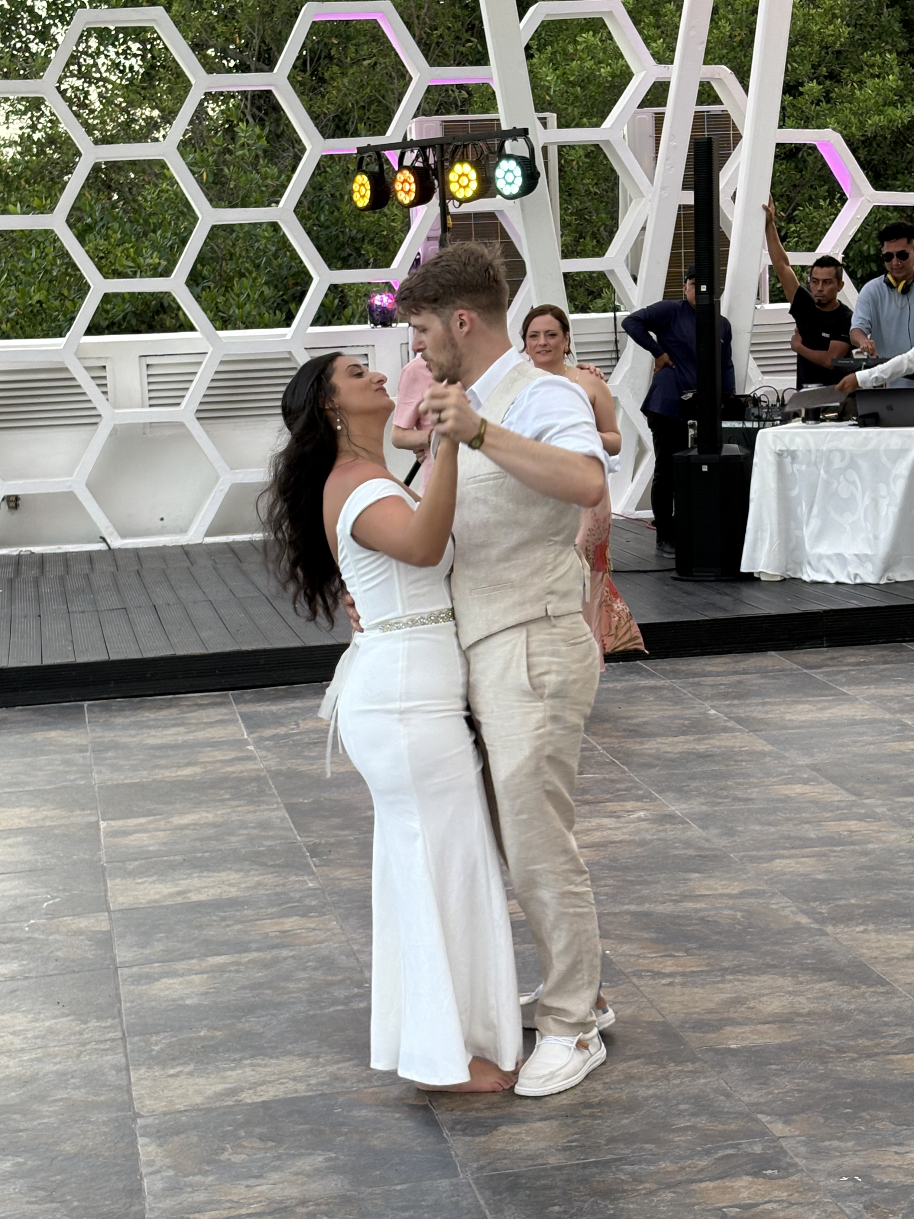 Aubrey and Noah dance in white attire on a tiled floor at an outdoor destination wedding.