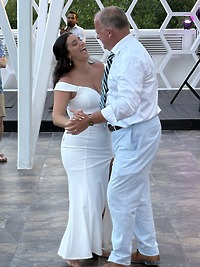 Aubrey and Noah share a joyful dance outdoors at their destination wedding, smiling together—she in a stunning white dress, he dressed smartly in a tie.