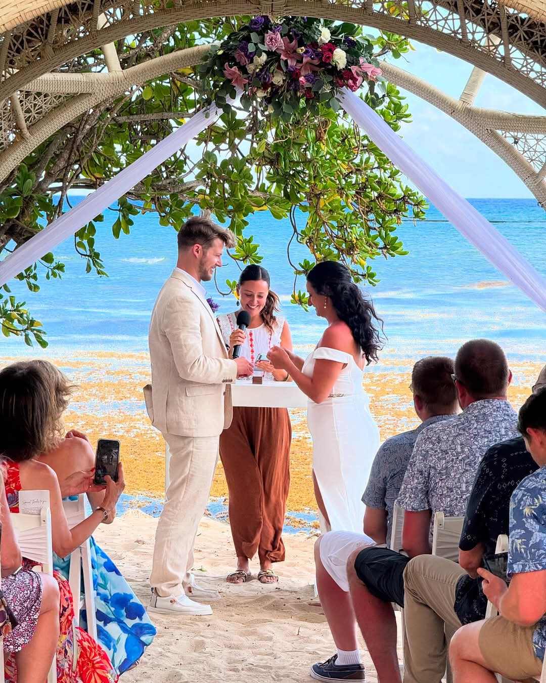 Aubrey and Noah exchange vows at their destination wedding on the beach, surrounded by guests seated nearby.