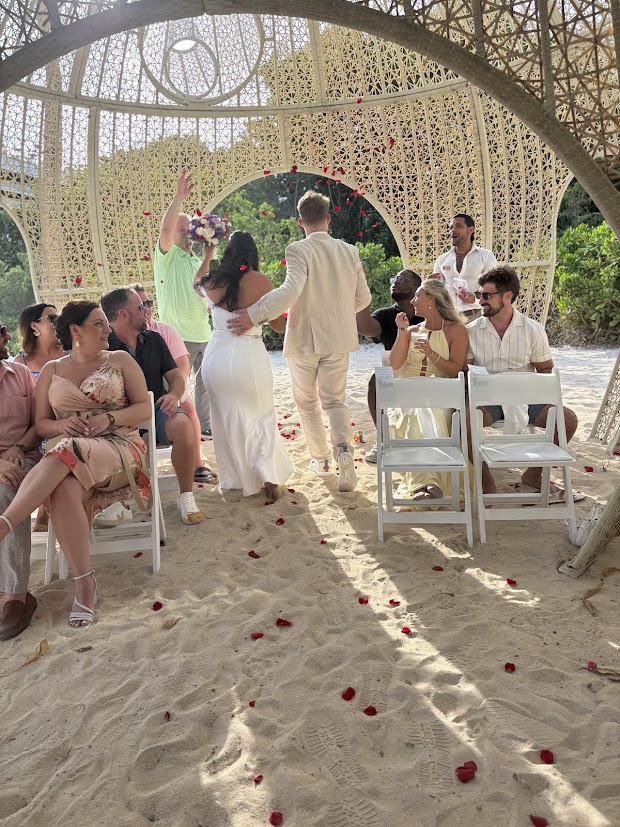 Aubrey and Noah: A beautiful destination wedding on a sandy beach, with seated guests and rose petals scattered along the aisle.