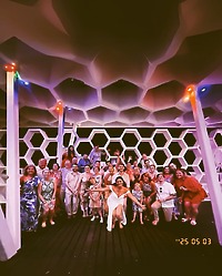 Sara and Tyler gather with a large group beneath a honeycomb-patterned ceiling at their destination wedding.